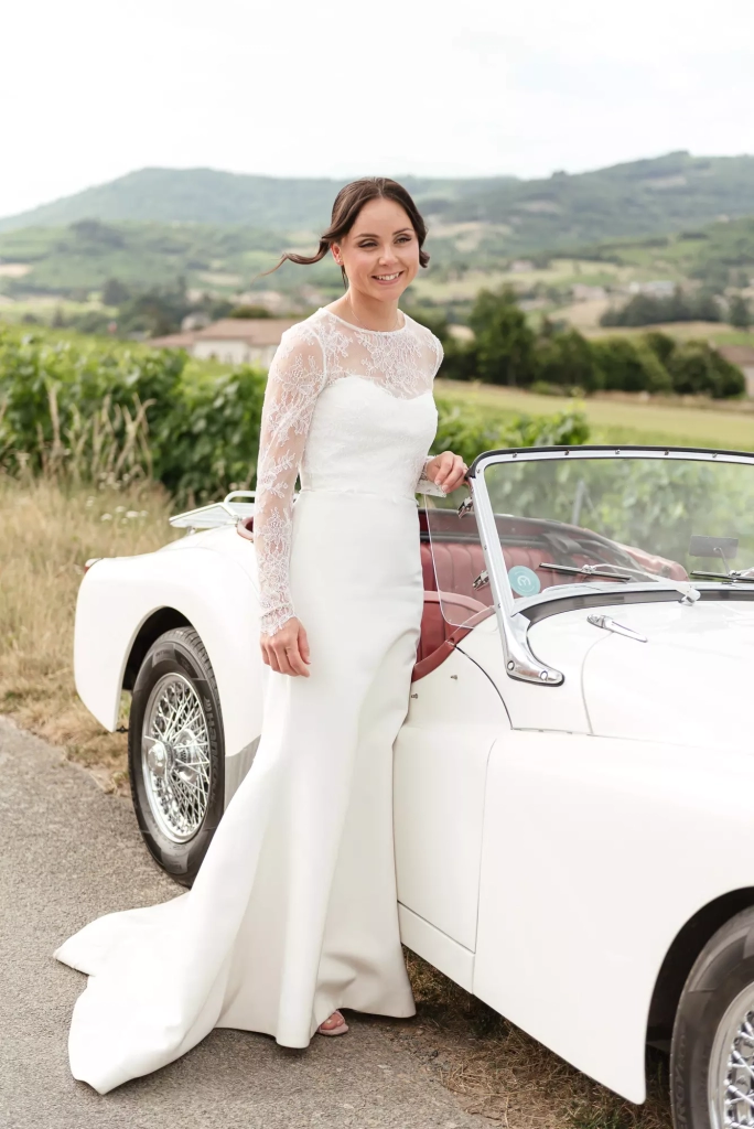 Bride standing beside a vintage car with the Beaujolais hills in the background