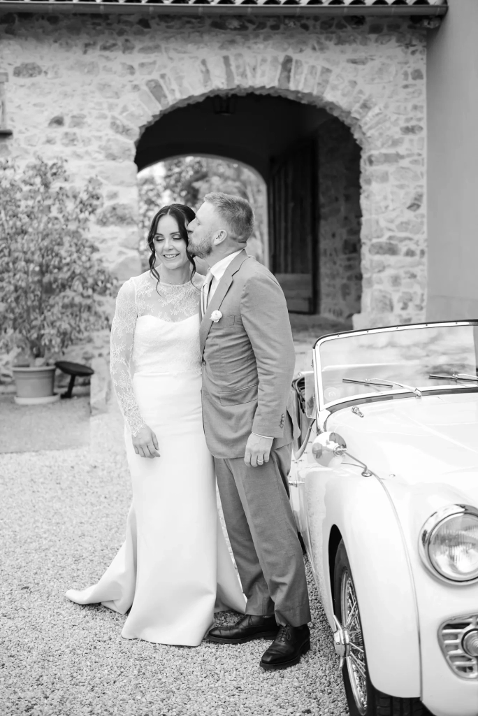 French-American newlyweds posing beside a vintage car at a château in Beaujolais